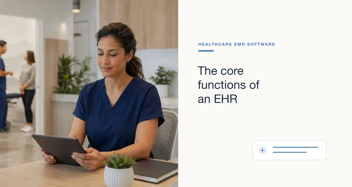 A clinician in navy scrubs works on a tablet at a front desk while colleagues talk in the background.